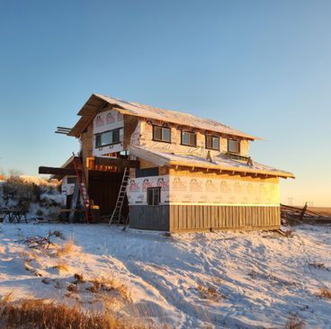 Snow-covered two-story house under construction in a rural winter field at sunset