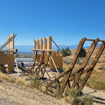 Wooden outdoor structures under construction in a dry field, with mountains in the background