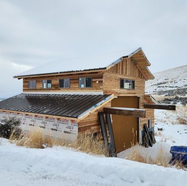 Wooden cabin under construction in snowy landscape with mountains in the background