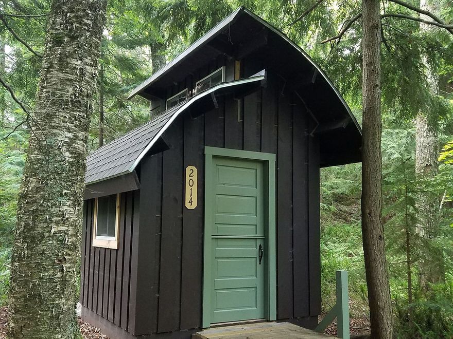 Small black wooden cabin with a green door in a forest.