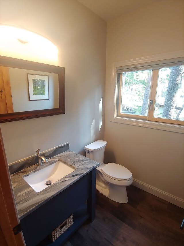 Small bathroom with vanity sink, mirror, toilet, and window, in beige and gray tones