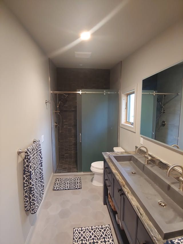 Modern bathroom with double sink vanity, shower, window, towel bars, and patterned floor mats.
