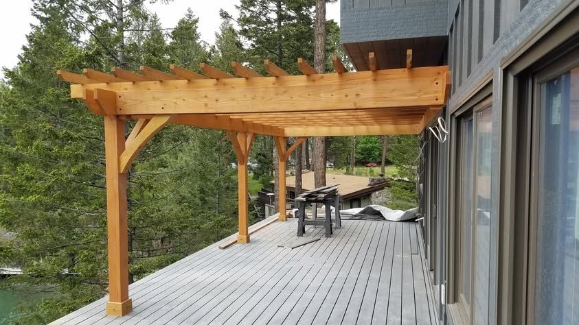 Wooden deck with pergola beside a modern house, overlooking trees and a forested landscape.