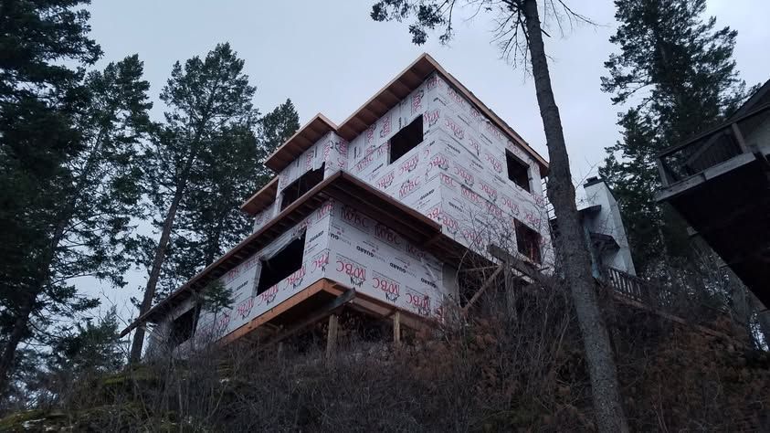 Abandoned house under construction on a hillside, with exposed framing and tall pine trees around it.