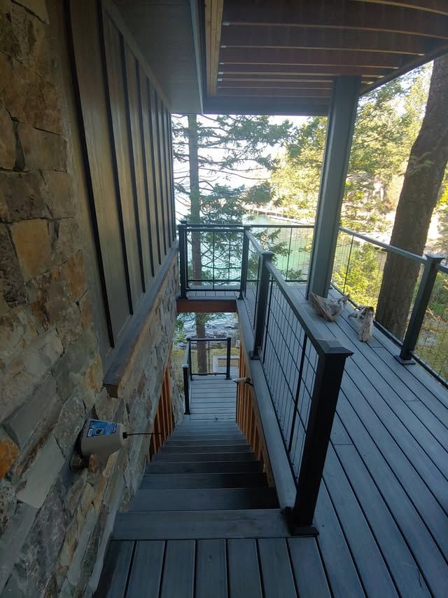 Stone stairway with black railings descending to a lower deck, surrounded by trees and a lake view