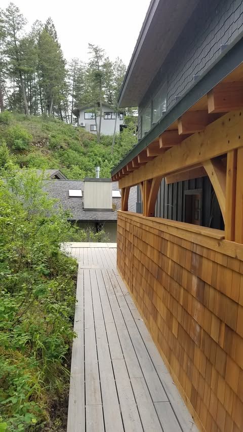 Wooden walkway beside a shingled building, overlooking trees and hillside homes.