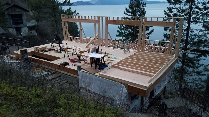 Wooden house frame under construction on a hillside overlooking water at dusk