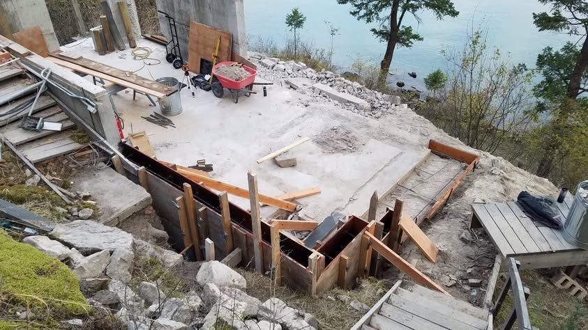 Snow-covered construction site with wooden foundation forms on a hillside by the water