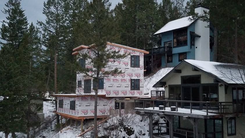 Snow-covered hillside lodge with pine trees and partially built buildings in a forested winter setting