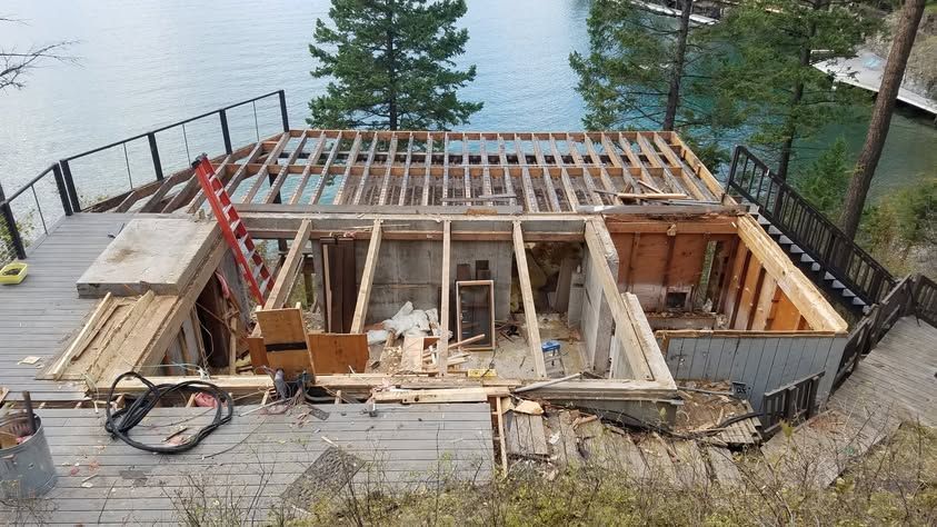 Construction site with a partially built wooden deck beside water, framed walls, and scattered tools