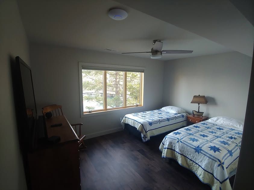Bedroom with two twin beds, window, ceiling fan, dresser, and chair on dark wood floor.