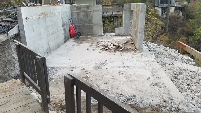 Partially built concrete structure with a rough floor, open gate, and debris on an outdoor hillside site