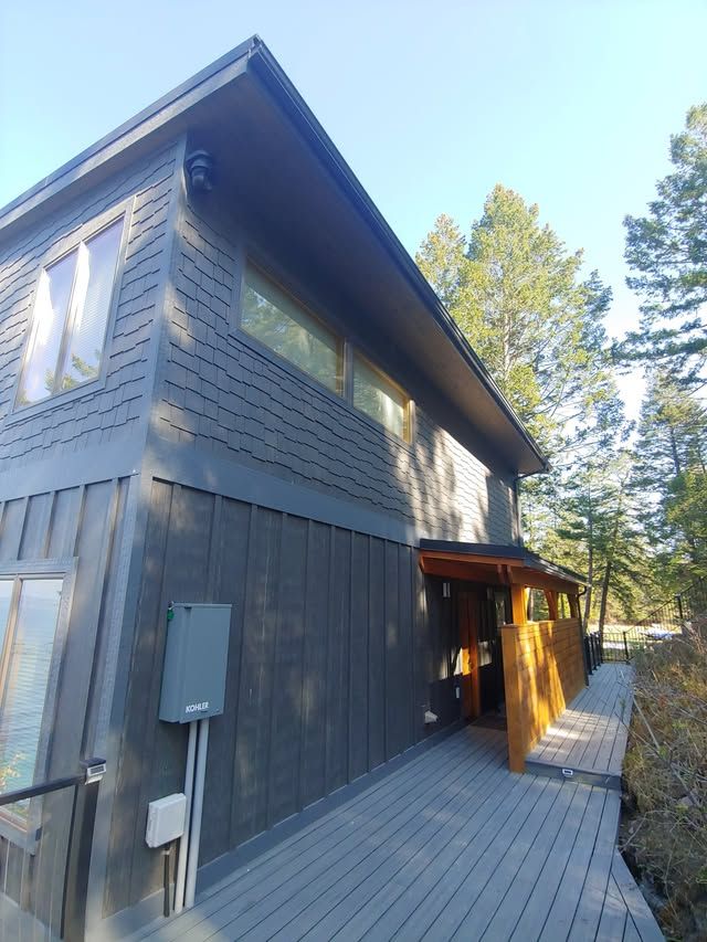 Modern dark gray two-story cabin with a wooden deck in a wooded setting