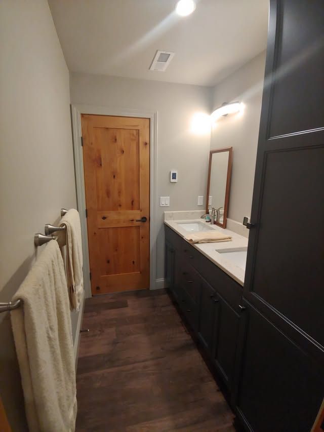 Narrow bathroom with wood door, dark vanity, wall mirror, and towel rack on the left.