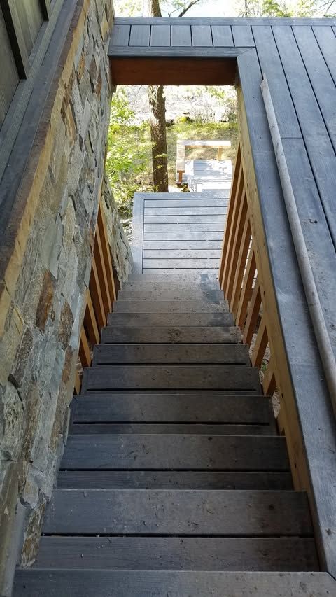 Wooden outdoor staircase descending to a lower deck with stone wall and railing on the left