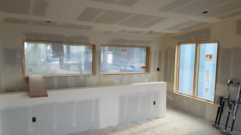 Unfinished room with drywall, large windows, and construction tools near a bright balcony door
