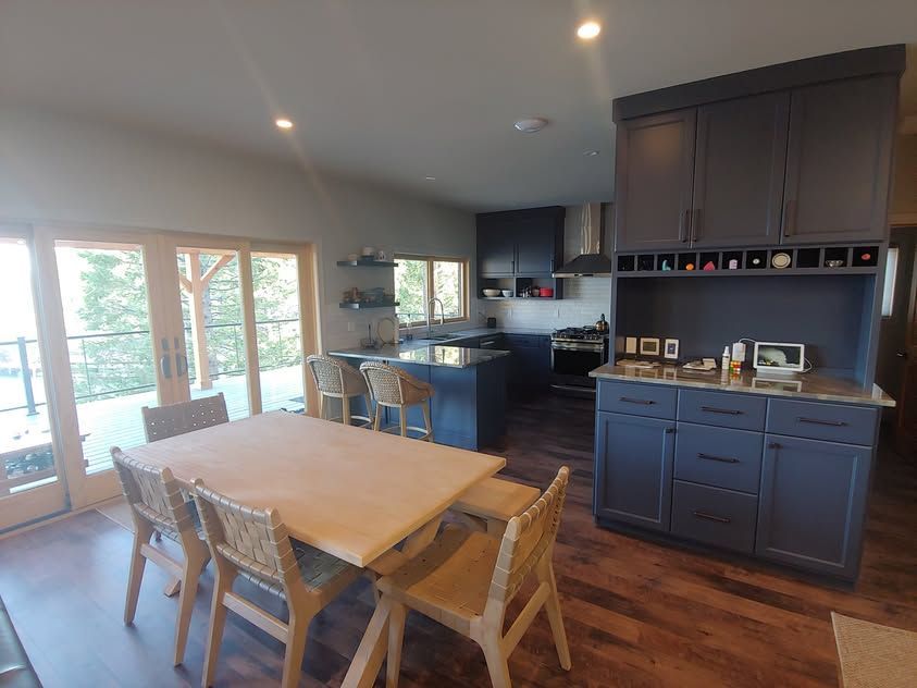 Modern kitchen and dining area with dark cabinets, wood floors, and a table by large windows