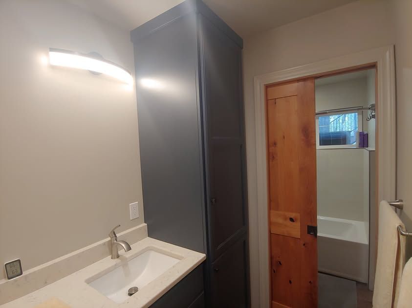 Small bathroom with white sink, tall dark cabinet, and an open door to a room beyond.