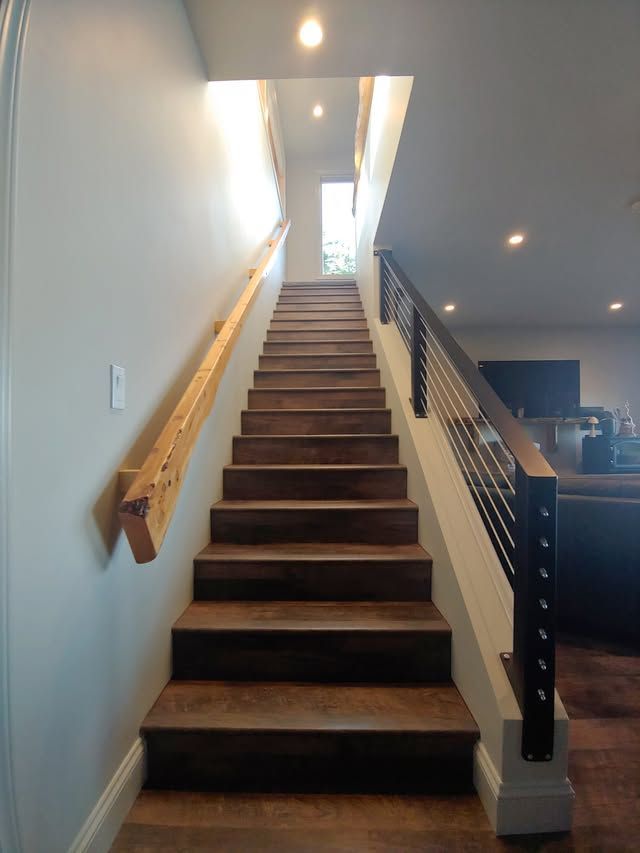 Indoor staircase with dark wood steps, white walls, and a wooden handrail leading to a bright upper landing