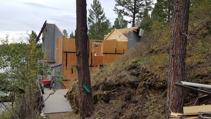 Partially built wooden house on a wooded hillside with trees and a narrow walkway