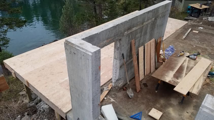 Partially built concrete wall beside water, with wooden planks and construction materials nearby