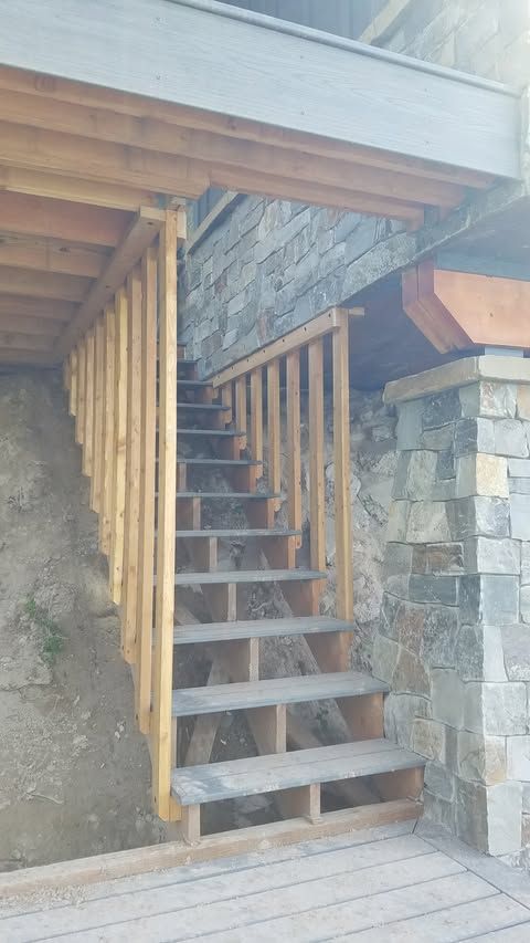 Stairway beside a stone wall, leading up to a wooden deck under an overhang.