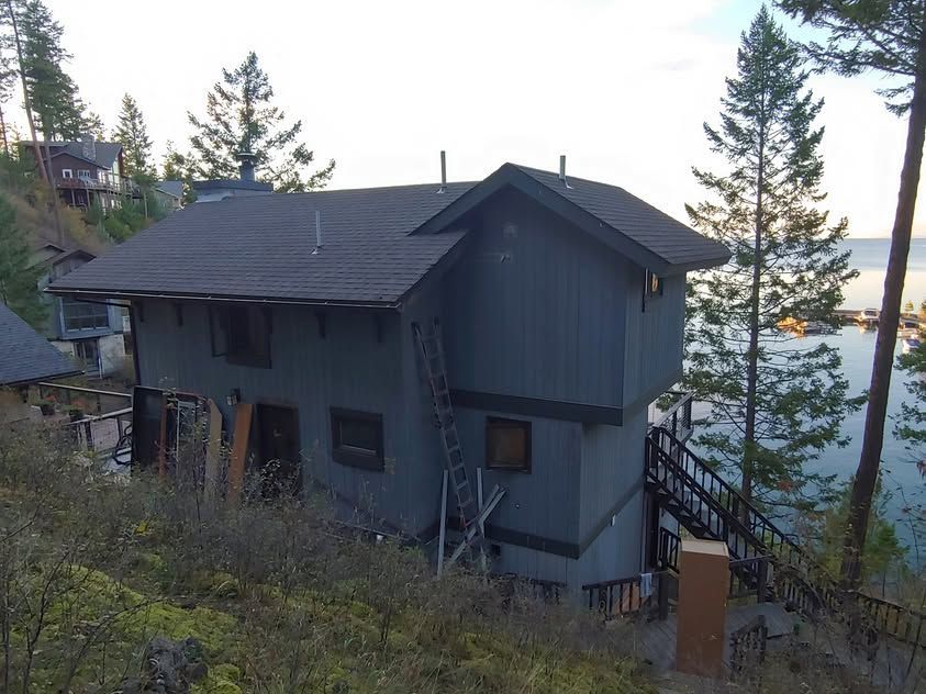 Gray lakeside house with deck and stairs among trees at sunset