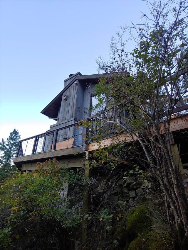 Wooden house on a steep hillside, with a balcony and trees in the foreground.