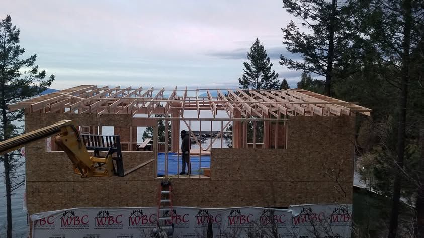 Partially built wooden house frame with roof trusses and construction materials at dusk