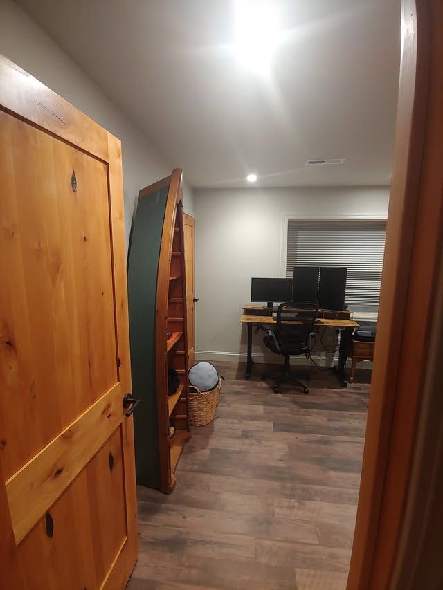 Small home office with desk, computer monitors, chair, and wood floor seen through an open door