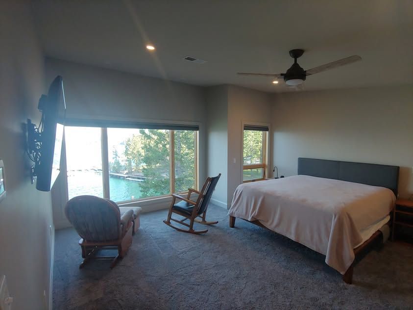Bedroom with large window, rocking chair, and bed in a modern room with carpet and ceiling fan