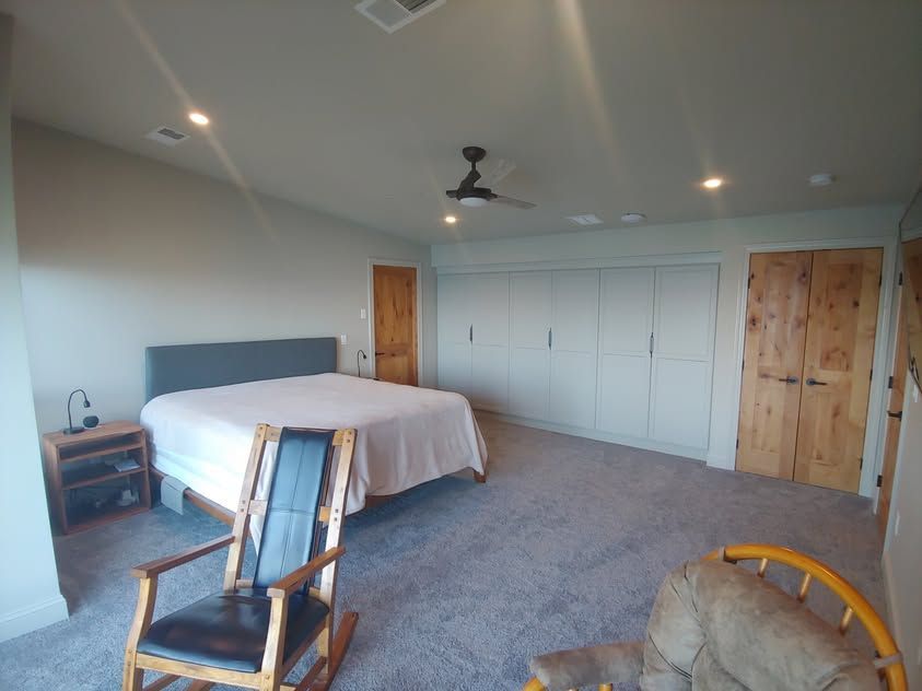 Spacious bedroom with a bed, gray carpet, white built-in closets, and wooden doors and chair.