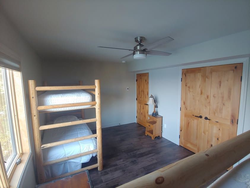 Small bedroom with bunk bed, wooden dresser, closet doors, ceiling fan, and a window on the left.