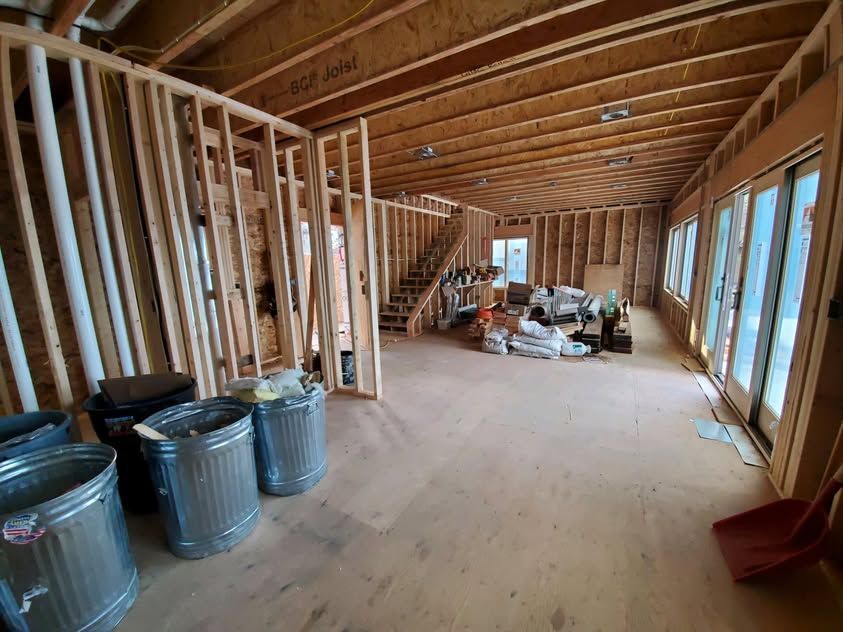 Unfinished attic room with exposed wood framing, trash bins on the left, and windows along the right wall