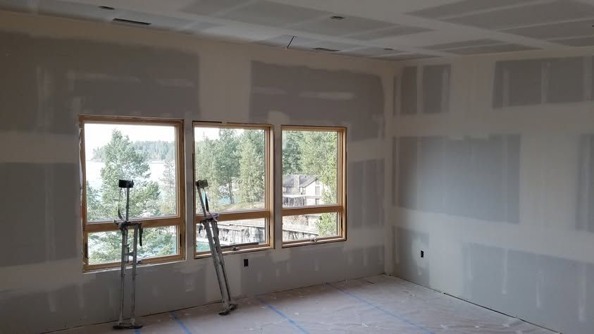 Unfinished room with drywall, three windows, and a ladder leaning near the wall.