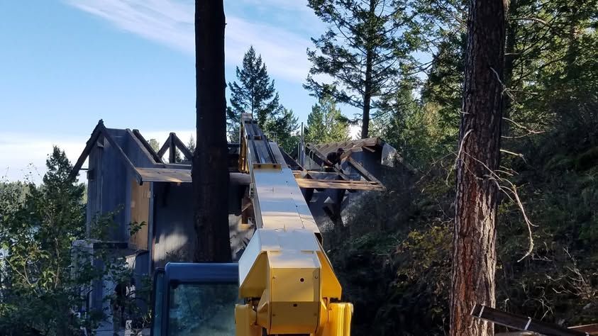Yellow crane lifting roof beams near a house in a forested mountain area