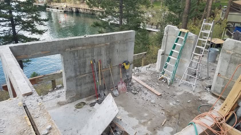 Partially built concrete structure beside a river, with ladders, scaffolding, and construction materials