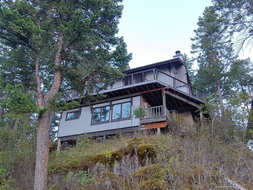 Wooden hillside cabin among tall trees, with a porch and large windows.