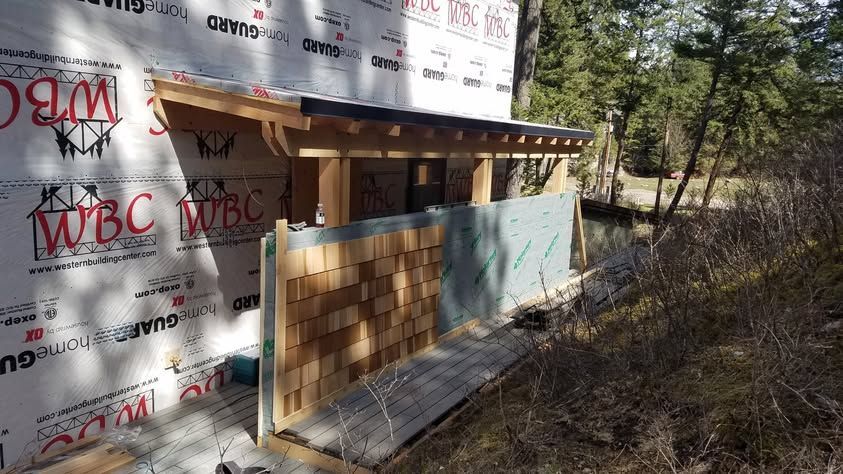 Partially built house with exposed framing, wood siding, and wrapped exterior in a wooded area