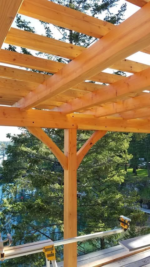 Wooden pergola beams under construction above a deck, overlooking a wooded hillside.
