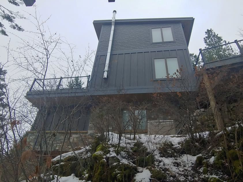 Gray house on a snowy hillside, viewed from below against an overcast sky.