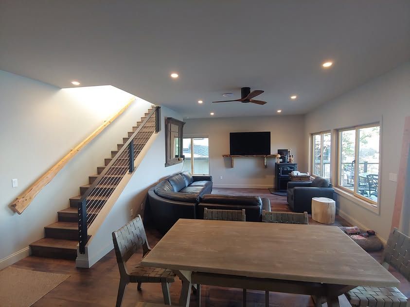 Open living room with staircase, leather seating, TV, and large windows overlooking a deck