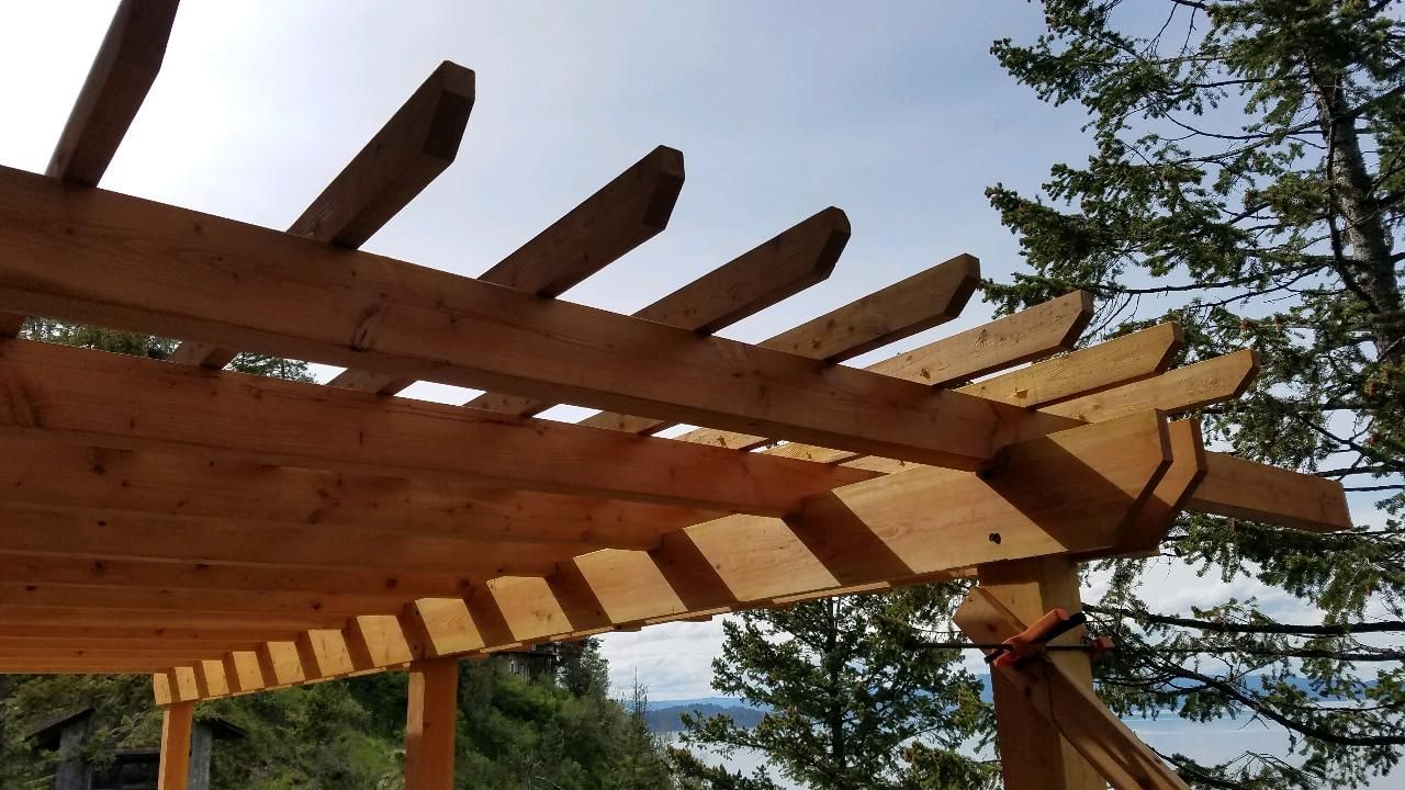 Wooden pergola frame with beams under construction against a blue sky and trees