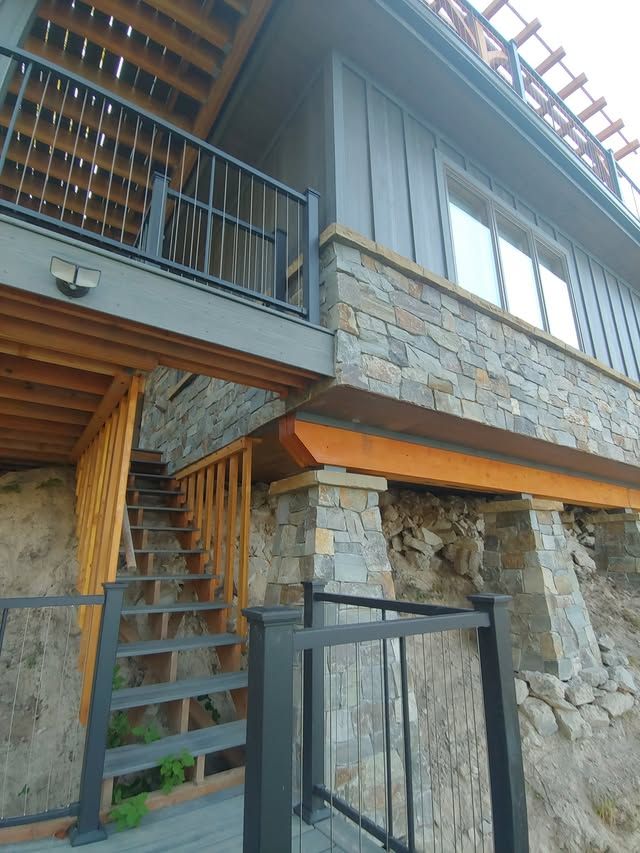 Stone-and-wood modern house exterior with stairs and balcony under overcast light