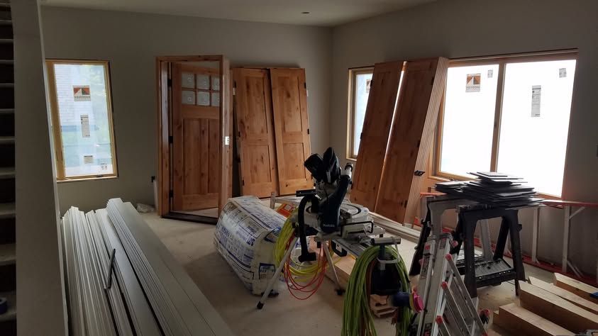 Unfinished room with drywall stacks, tools, and wood boards near bright windows and double doors