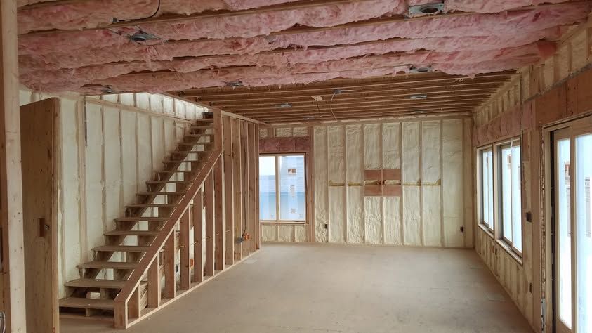 Unfinished room with exposed wood framing, pink insulation ceiling, staircase, and windows on the right.