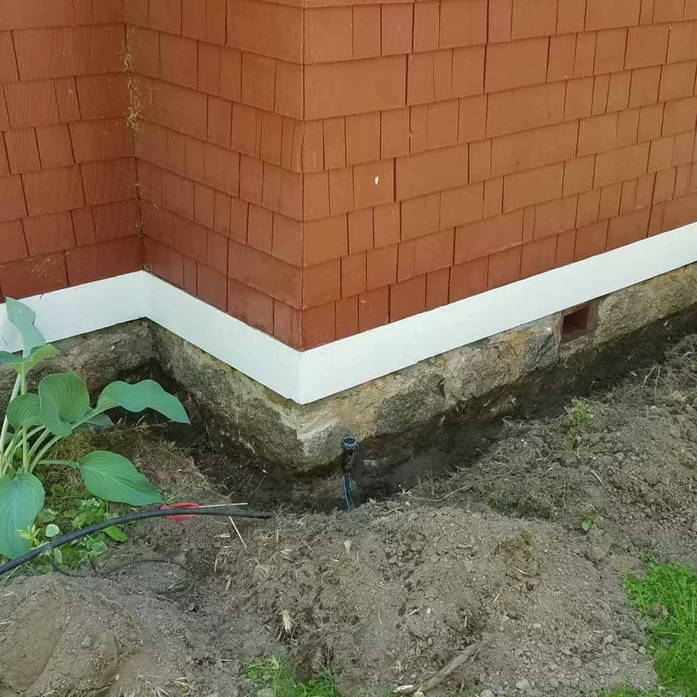Exterior corner of a brick house with a white foundation trim and muddy ground below