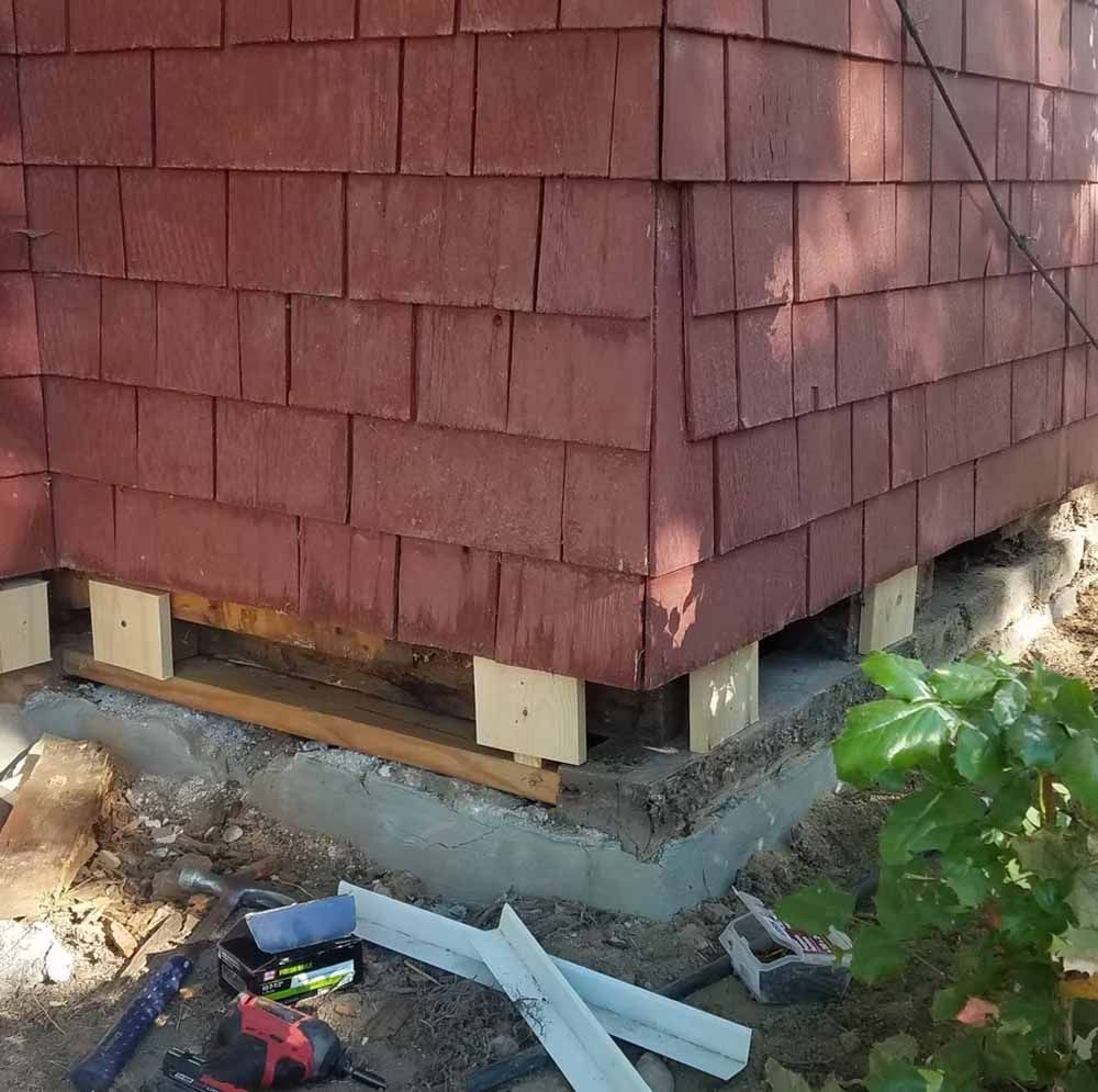 House corner on new concrete foundation with wooden shims and construction debris nearby