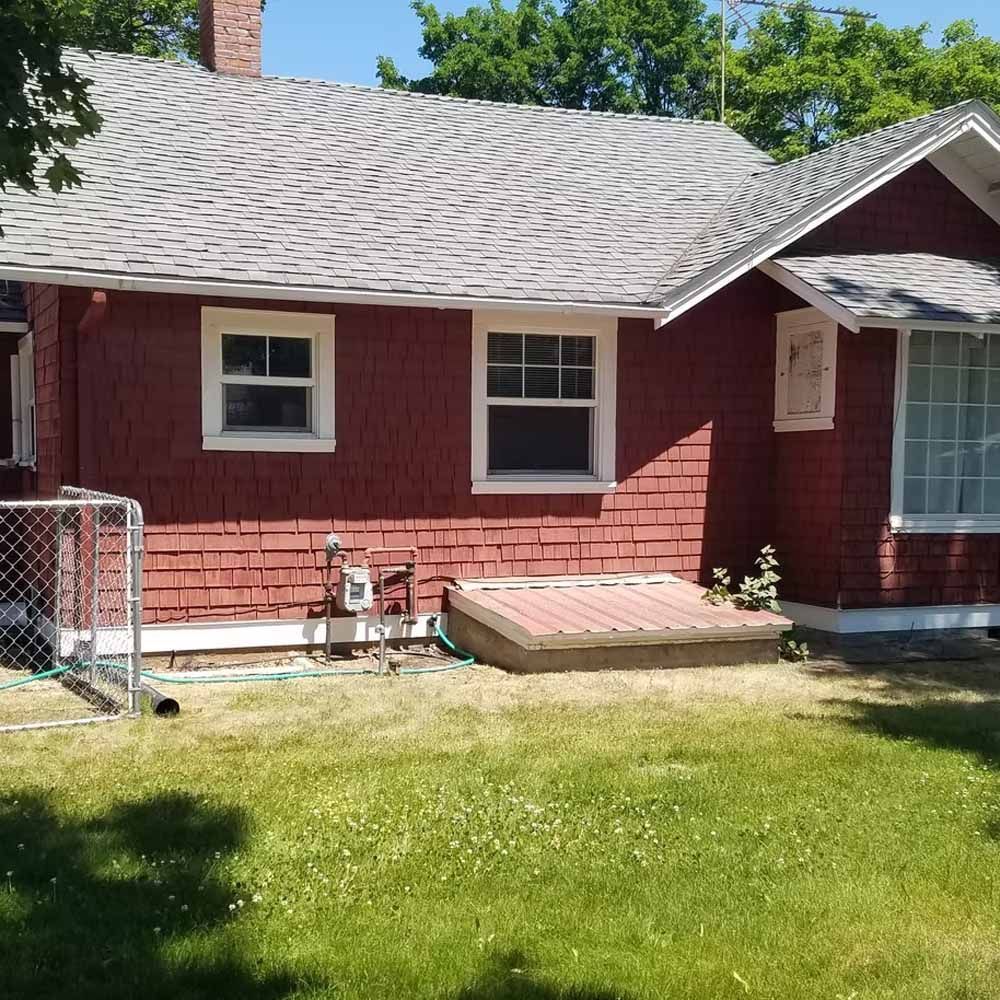 Red house exterior with gray shingle roof, small windows, and a grassy yard in front.