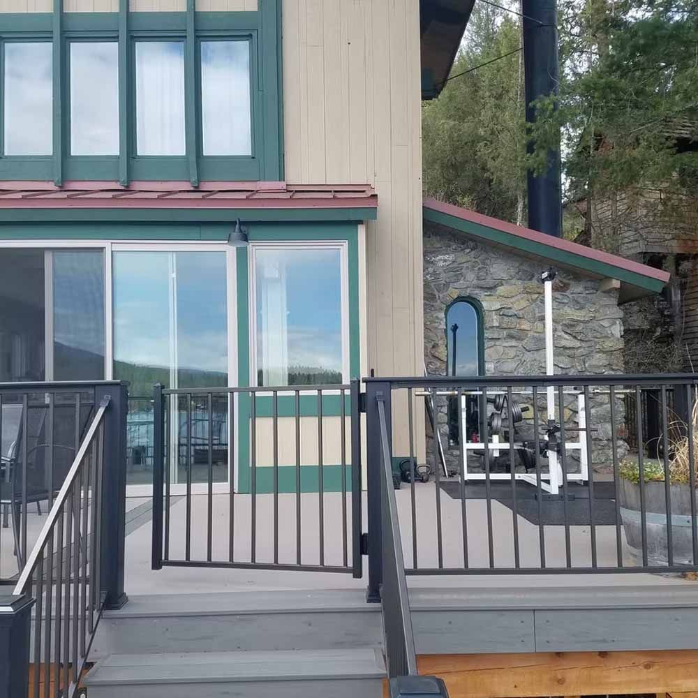 Modern building deck with black railings, sliding glass doors, and a stone wall by a wooded area